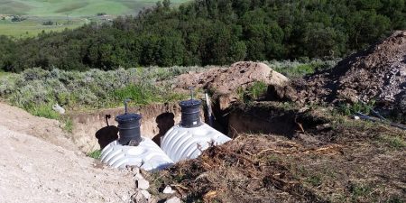 Two large white water tanks are partially buried in the ground, with pipes and surrounding soil indicating an ongoing installation process.