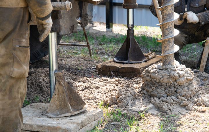 Workers are engaged in drilling operations, using equipment to excavate soil and create a foundation or well structure.