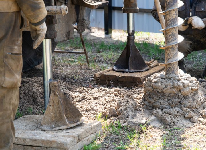 Workers are engaged in drilling operations, using equipment to excavate soil and create a foundation or well structure.