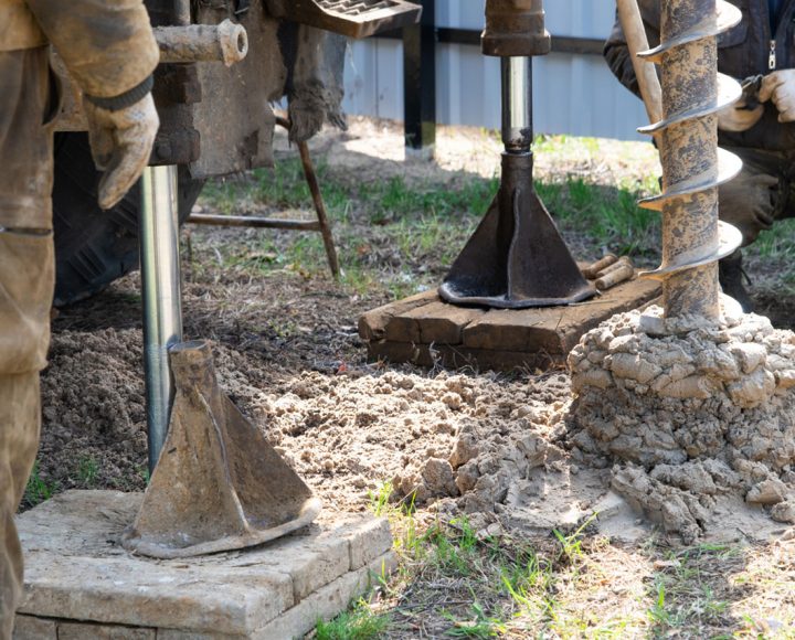Workers are engaged in drilling operations, using equipment to excavate soil and create a foundation or well structure.