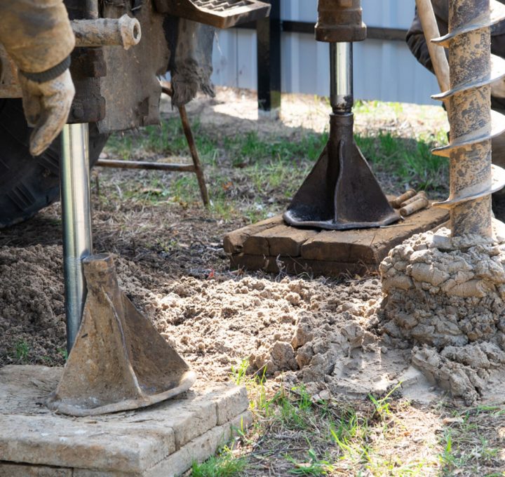 Workers are engaged in drilling operations, using equipment to excavate soil and create a foundation or well structure.