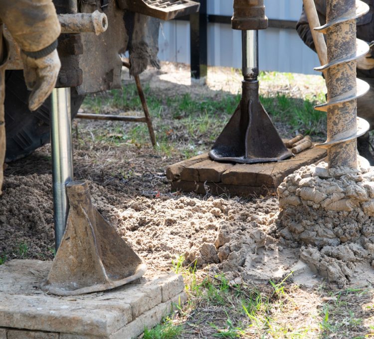 Workers are engaged in drilling operations, using equipment to excavate soil and create a foundation or well structure.