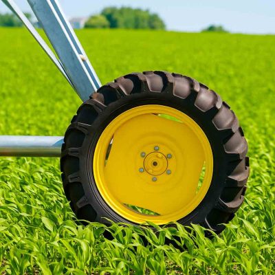 A close-up view of a large agricultural tire with a yellow rim, attached to machinery, set against a backdrop of lush green crops.