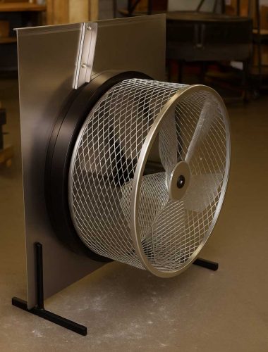 A large industrial fan unit with a metallic mesh cover is displayed in a warehouse setting, showcasing its robust design.