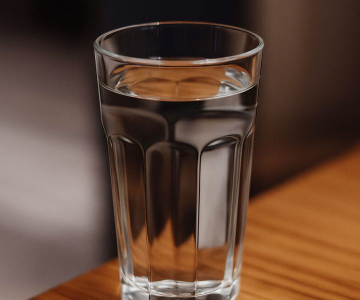 A clear glass filled with fresh water sits on a wooden table, emphasizing purity and hydration.