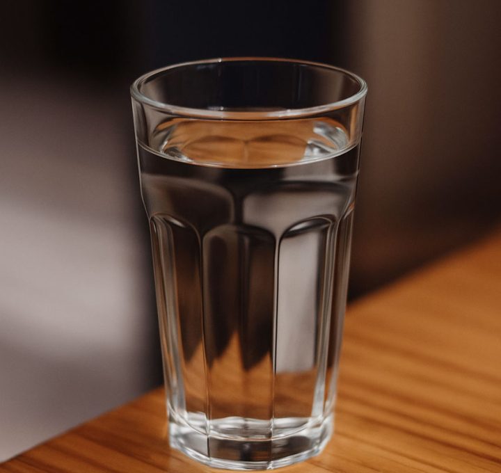 A clear glass filled with fresh water sits on a wooden table, emphasizing purity and hydration.