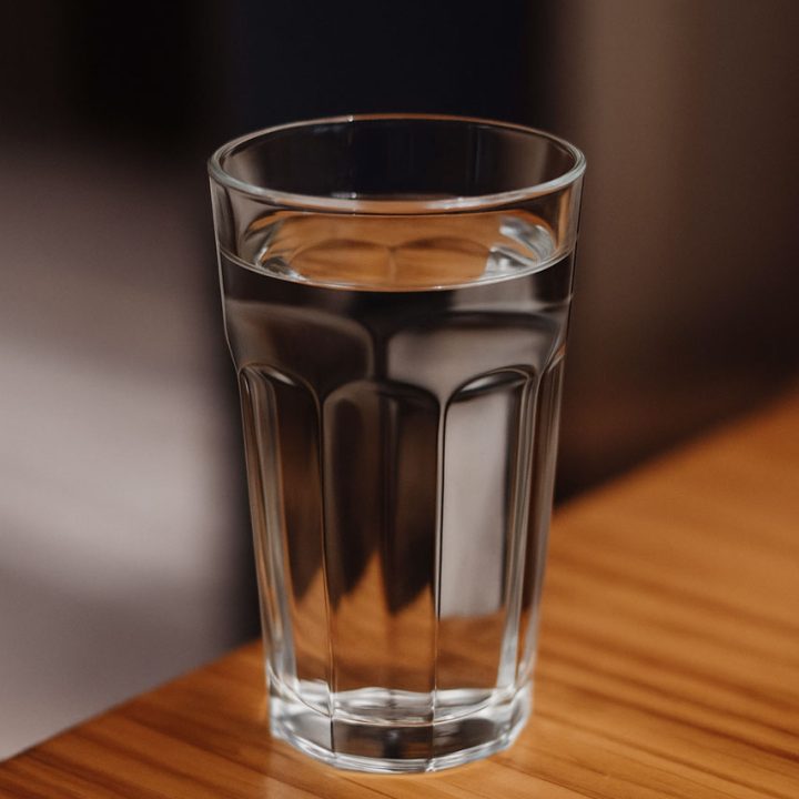 A clear glass filled with fresh water sits on a wooden table, emphasizing purity and hydration.
