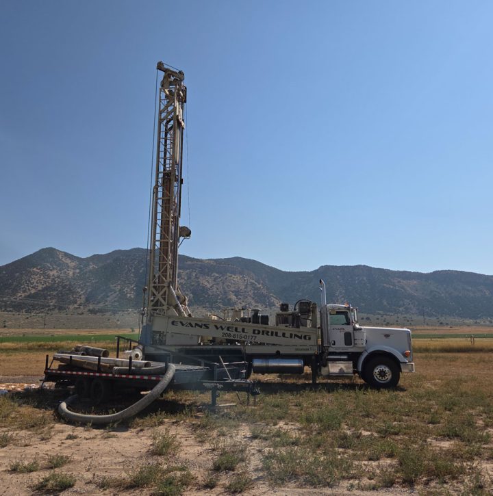 A full view of an Evans Well Drilling truck set up in a vast, arid landscape, with a trailer attached and mountains visible in the distance.