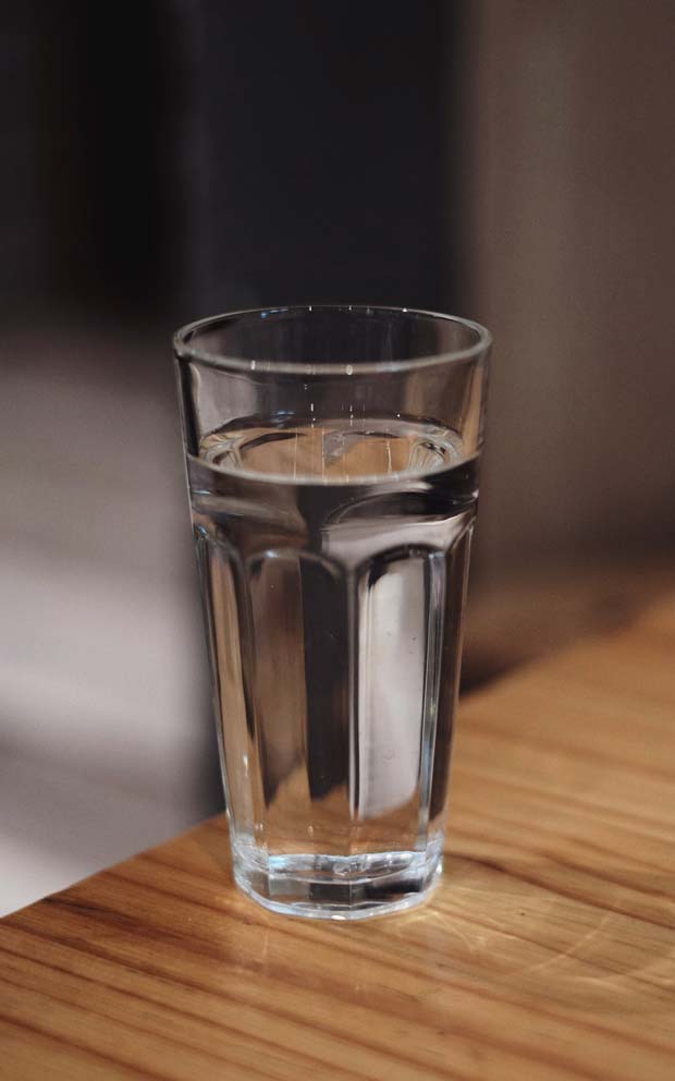 A clear glass filled with water is placed on a wooden table, set against a softly lit background.
