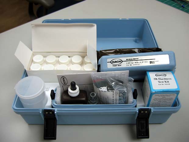 A blue water hardness test kit is open on a table, revealing bottles of distilled water, tablets, and other testing materials.