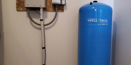 A VFD conversion unit is mounted on a wall next to a blue water storage tank, indicating an upgrade for efficient water pumping.