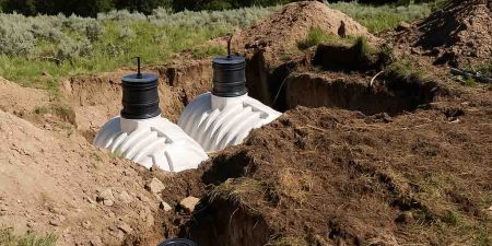 White water storage tanks are being installed in a dug-out trench, set against a backdrop of greenery and rolling hills.