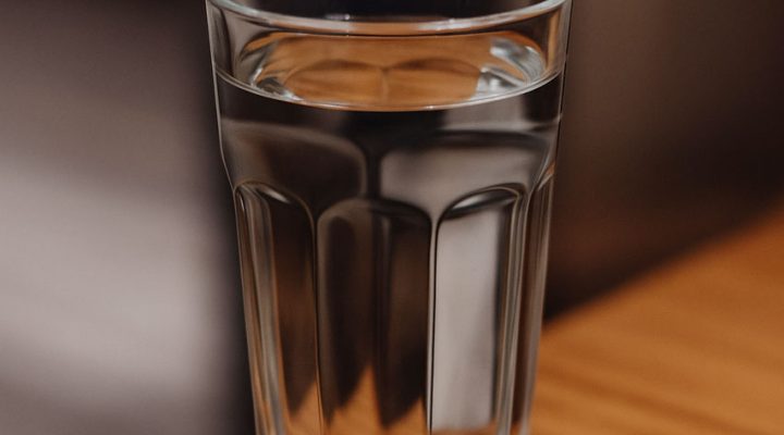 A clear glass filled with fresh water sits on a wooden table, emphasizing purity and hydration.