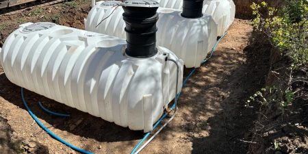Multiple large white storage tanks are installed outdoors, connected by pipes, likely for water storage or treatment purposes.